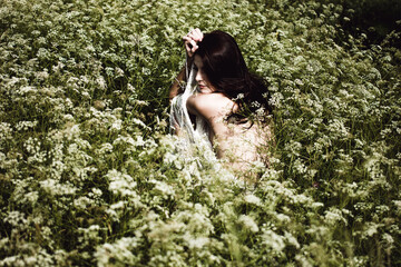 Young woman with black hair and naked back among wildflowers	
