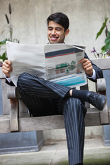Happy Indian businessman reading newspaper while sitting on bench