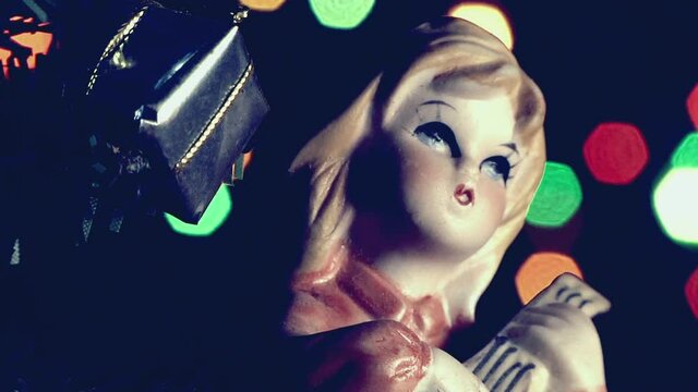 Natale vintage, bambola bambina che suona vicino l'albero di Natale con luci a intermittenza colorate.
