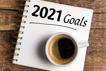 New year goals 2021 on desk. 2021 goals list with notebook, coffee cup on wooden background. Goals, plan, strategy, business, idea, action concept. Top view