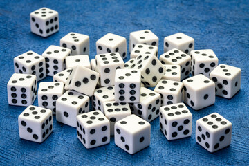 pile of white cubic dice with black pips (dots) against blue handmade paper, game, gamble, chance and risk concept