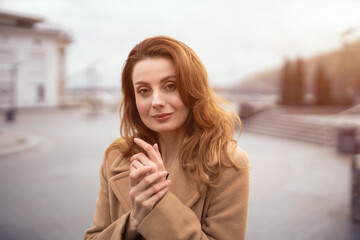 Stroking hands to warm up charming young woman standing on the street. Portrait of stylish young woman wearing autumn coat outdoors. Autumn accessories. 