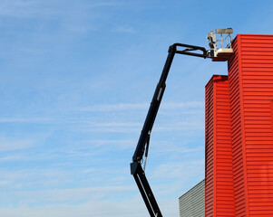 Fototapeta premium Long black boom of aerial work platform on a modern red aluminium facade. No people, copy space.