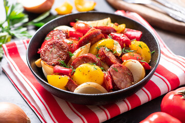 Sausages fried with peppers, tomatoes, and onions in a black plate on a dark background close-up. Sausages stewed with vegetables. Traditional Hungarian food lecho.