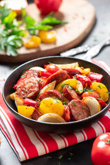 Sausages fried with peppers, tomatoes, and onions in a black plate on a dark background close-up. Sausages stewed with vegetables. Traditional Hungarian food lecho.