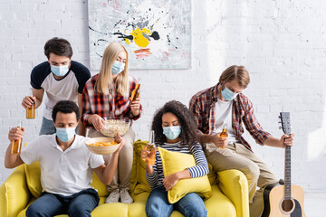 multicultural friends in medical masks holding beer and snacks with closed eyes during party