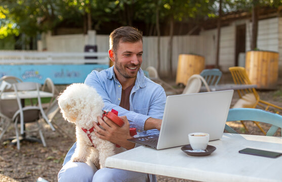 The young man is working on a laptop outside with a puppy in his lap.