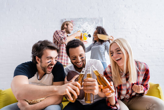 excited man screaming while clinking beer bottles with multicultural friends with painted faces