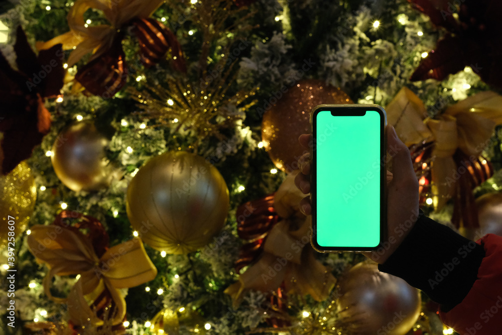 Wall mural close up one hand showing green screen mobile phone in front of Christmas tree at night