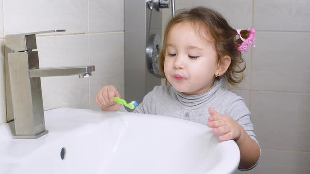 Cute girl in the bathroom clumsily brushing her teeth and spitting in the sink
