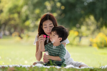 Asian family having fun mother and her son playing with soap bubbles in the park together