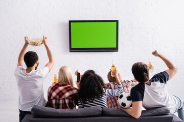 back view of multicultural football fans watching championship on tv and showing winner gesture