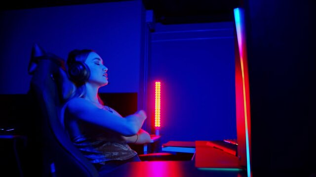 Tattooed young woman sitting in neon gaming club - playing game and gets dissapointed