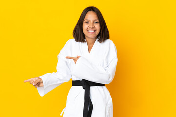 Young woman doing karate isolated on yellow background surprised and pointing side