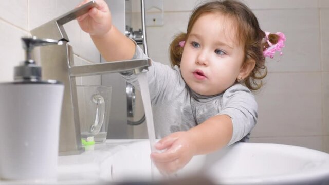 Cute little girl in the bathroom clumsily washes her hands and face