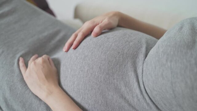 asian pregnant woman touching belly with care and baby in abdomen moving.