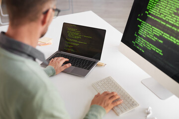 Rear view of mature programmer sitting at the table developing program on a desktop computer