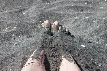 A man's feet are covered in black magnetic sand on the beach. Useful sand baths.