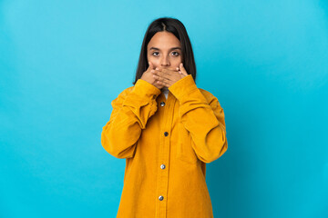 Young latin woman isolated on blue background covering mouth with hands