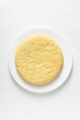 Spanish omelette in a round white plate on white background. Senital view. Vertical picture