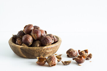 Close up of soap nuts in a wooden bowl on white background; natural laundry detergent; eco friendly alternative 
