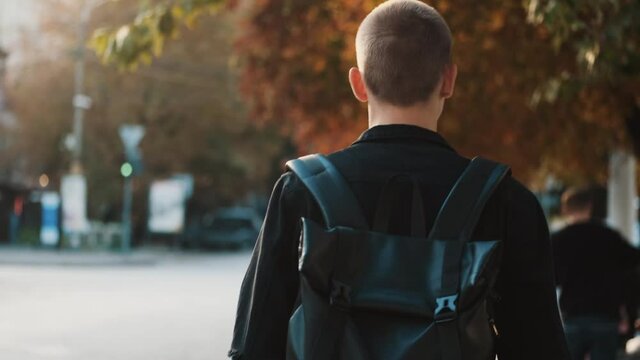 Attractive student guy with backpack going home after study in university. Young student walking through city street