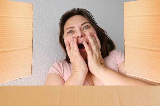 Woman Opened A Cardboard Box With An Ordered Product And Emotionally Reacts To Its Contents, The Concept Of A Postal Item, A Package, Buying Goods Online, Surprises