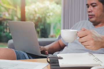 A man in casual wear picks up a cup of coffee while he is working at home office.