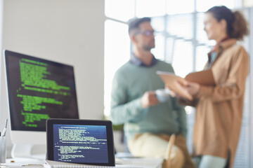 Image of digital tablet and computer on the table with people talking to each other in the background at office