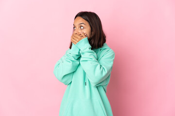 Young latin woman isolated on pink background covering mouth and looking to the side