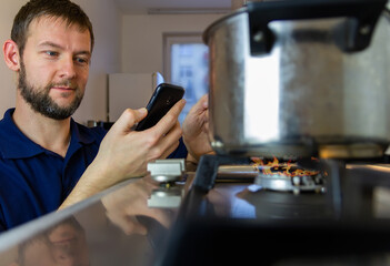 Young caucasian man happy, easy cooking in home kitchen with mobile phone. Man making home works with smart house