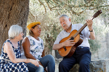 Anziano signore Ottantenne suona una serenata a due anziane signore seduti sotto un albero di ulivo...