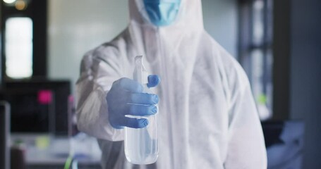 Health worker wearing protective clothes and face mask spraying disinfectant at modern office - Powered by Adobe