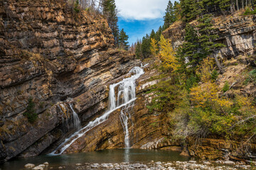 Cameron falls in autumn sunny day morning. Blue sky, white clouds over mountains in the background. Waterton Lakes National Park, Alberta, Canada.