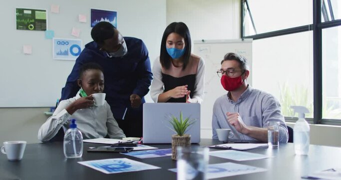 Office colleagues wearing face masks using laptop together in meeting room at modern office