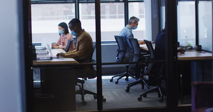 Office colleagues wearing face masks working while sitting on their desks at modern office