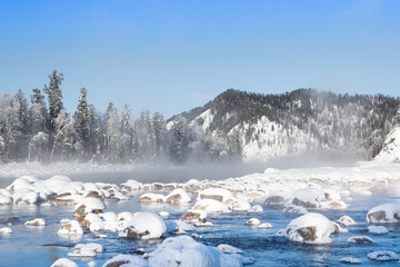 Boulders in cold water are covered with snow. Winter river on frosty morning.