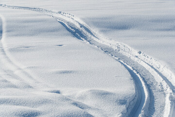 Snowmobile tracks in deep snow. Twisting traces of a snowmobile crossing snow covered field - 397266819