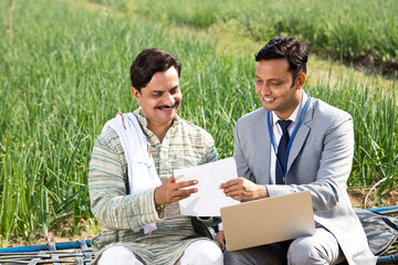Farmer with businessman using laptop on agriculture field