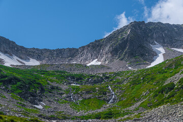 Rock ridge with snow and stone placers under blue sky. Summer trip to mountain valley. Atmospheric...