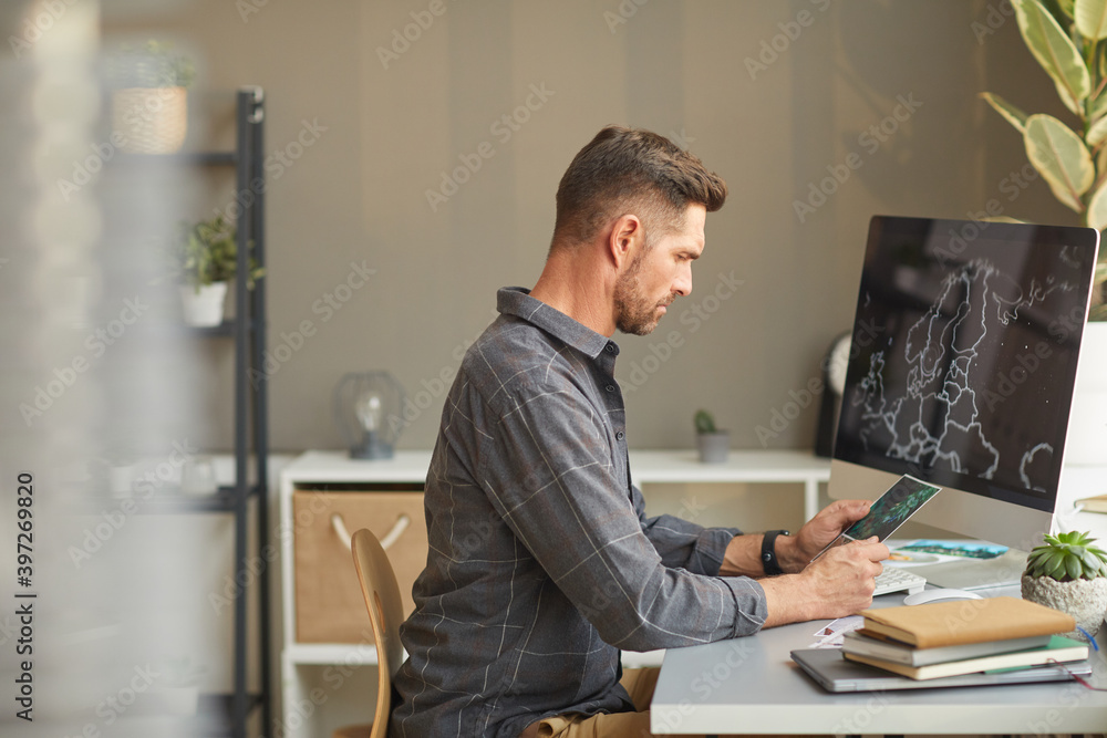 Wall mural serious graphic designer sitting at the table in front of computer and working at office