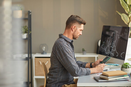 Serious graphic designer sitting at the table in front of computer and working at office