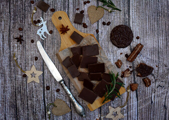 Pieces of dark chocolate on a cutting board and New Year's decor on a rustic background. View from above