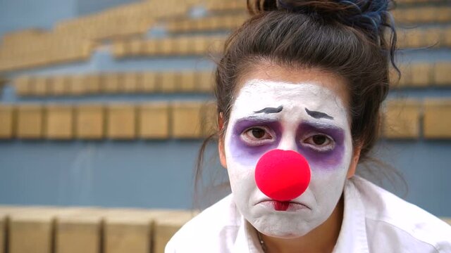 Sad clown with white face and red nose looking at camera