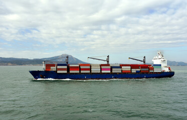 Fully loaded, geared container ship departing port of Xiamen, China. 