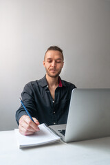 Caucasian Man is Seriously Working on his Laptop and Writing in a Notebook, in Quarantine for the Coronavirus Pandemic