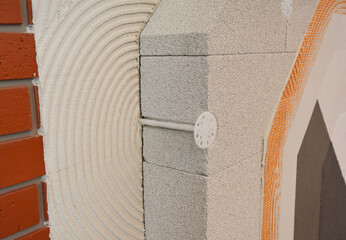 Cross-section view of brick house insulated wall construction with internal plastering, concrete aerated hollow block, thermal insulation, fiberglass reinforcing mesh and external plastering layers.