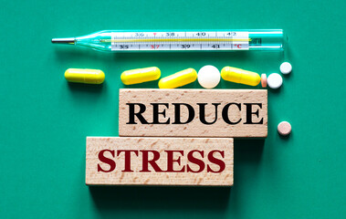 REDUCE STRESS - text on wooden bars on the background of a thermometer and pills