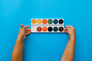 child hands holding a watercolor on a blue background
