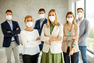 Business team members standing iwith protective facial masks and looking at the camera